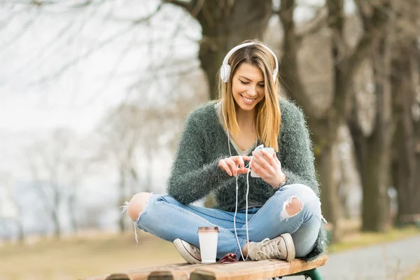 Cool duizendjarige teenaage meisje in park in het najaar met hoofdtelefoons en slimme telefoon — Stockfoto