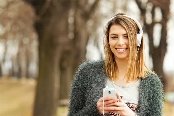Menina adolescente milenar com fones de ouvido e telefone inteligente no parque no outono — Fotografia de Stock