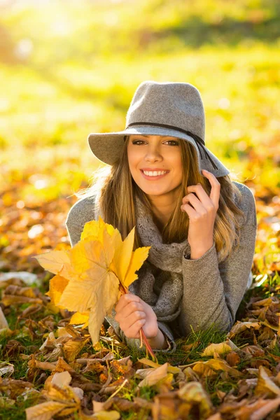 Bella giovane donna in cappello grigio floppy nel parco che tiene foglie — Foto Stock