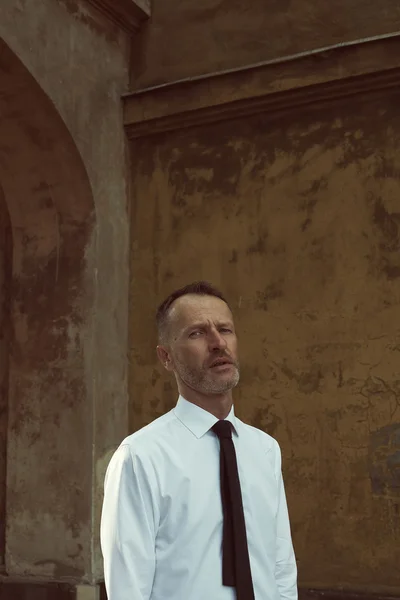 Smart casual handsome mature man stands over old house walls — Stock Photo, Image