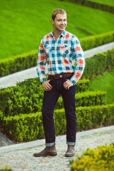 Retrato de feliz joven feliz hombre posando cerca de césped verde en el parque —  Fotos de Stock