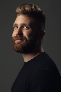 Her yaşta müthiştir. 35 yaşındaki gülümseyen adamın portresi gri arka planda siyah tişörtle poz veriyor. Kapatın. Hippi tarzı. Kızıl saçlı, modern saç kesimli. Stüdyo çekimi
