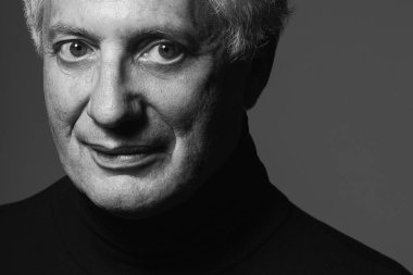 Asla yaşlanma, yakışıklı, her yaş kavramında seksi olma. Gri arka planda siyah balıkçı yaka giyen modaya uygun olgun bir adamın portresi. Modern saç kesimi. Gümüş saç.