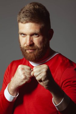 Gri duvarda savaşmaya hazır, orta yaşlı, gururlu, kızıl saçlı bir sporcunun portresi. Kırmızı spor giyim. Futbolcu. Oduncu tarzı. Dikey stüdyo çekimi