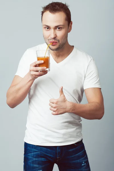 Lustiges Porträt eines lächelnden jungen Mannes mit braunen Augen, der frischen Saft trinkt Stockbild