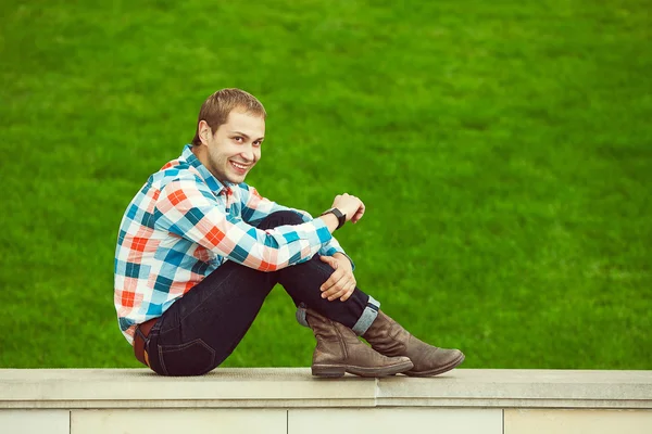 Retrato de feliz jovem feliz homem relaxante perto de gramado verde — Fotografia de Stock