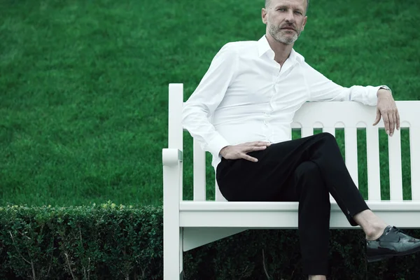 Men fashion concept. Portrait of mature charismatic man sitting on bench — Stock Photo, Image