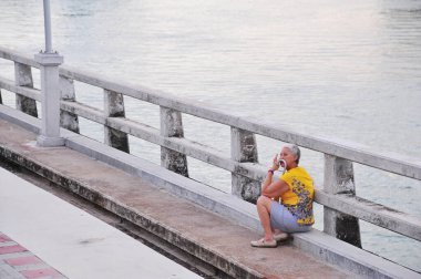 Yaşlı Asyalı kadın beton köprüde dinleniyor.