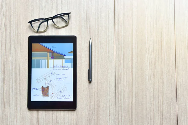 a tablet showing sketch of architectural drawing design detail with digital pens on wood table, the concept of new technology for working of tablet with pen and eyeglasses