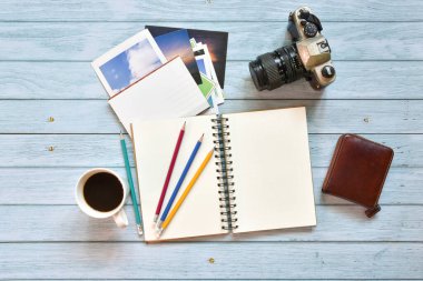Hayat, gezgin not kavramı, klasik film kamerası, kartpostal kahve fincanı ve mavi gökyüzü ahşap arka planında boş sayfaları olan renkli kalem içeren açık not defteri görüntüsü.