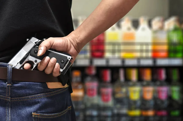 A man pulls out a gun tucked in his pant rear view with blurred department store background, a concept of city crime social issue