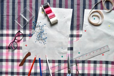 Kumaş, dikiş ipliği, makas, gözlük, renkli kalem, cetvel, santimetre bant, iplik ve ekipman makarası üzerine dikiş malzemeleri.