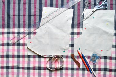 Kumaş, dikiş ipliği, makas, renkli kalem, kalem, cetvel, santimetre bant, iplik ve ekipman makarası üzerine dikiş malzemeleri.