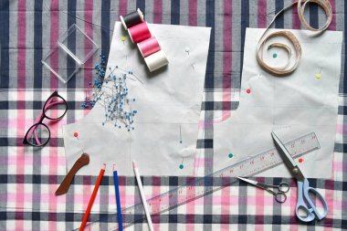 Kumaş, dikiş ipliği, makas, renkli kalem, kalem, cetvel, santimetre bant, iplik ve ekipman makarası üzerine dikiş malzemeleri.
