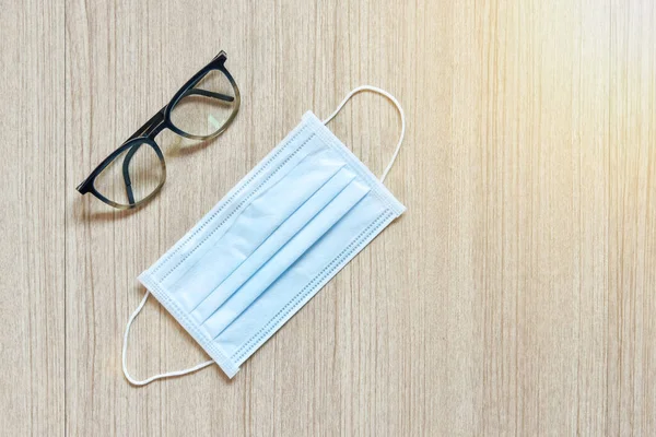 Clear eyeglasses and protection mask, Glasses transparent dark blue frame with protection paper mask on a wooden background, a concept of virus and pollution protection with copy space