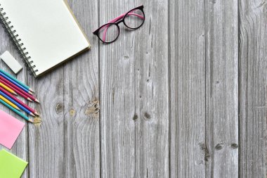 Hayat, iş yeri malzemeleri veya eğitim konsepti, açık defterin üst görünümü ve eski kahverengi ahşap üzerine boş sayfaları olan çeşitli renkli kalemler ve gözlükler, metin eklemeye hazır.