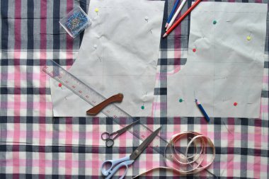 Kumaş, dikiş ipliği, makas, renkli kalem, kalem, cetvel, santimetre bant, iplik ve ekipman makarası üzerine dikiş malzemeleri.