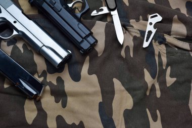 Kartuş şarjörlü siyah ve krom tabanca, küçük bıçak ve kamuflaj asker pantolonu üzerinde çok işlevli cep aleti, çeşitli taktiksel silah ve savunma araçları