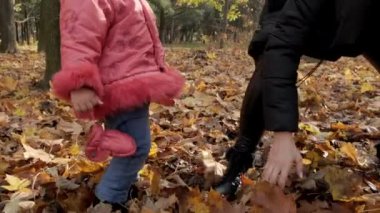 Genç bir kadın ve küçük kızı, şehir parkına sarı sonbahar yaprakları fırlatıyorlar. Yavaş çekim.