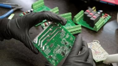 Professional master in black gloves examines electrical board in hands for repair. Close-up.