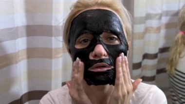 Yüzüne siyah maske takan genç bir kadın. Cilt tazeleme ve sağlık. Yavaş çekim.