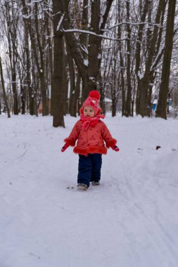 Kırmızı ceketli bebek ormanda kar altında yürüyor..