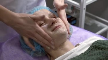 Güzellik uzmanının yakın çekimi kremi müşterinin yüzüne masaj hareketleriyle uyguluyor. Kozmetoloji prosedürleri.