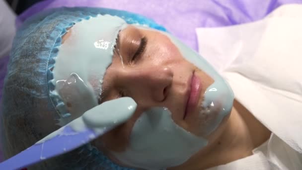 Zbliżenie kosmetyczka stosuje alginianową maskę twarzy do młodej kobiety. — Wideo stockowe