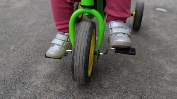 Крупный план малышки, которая едет на трехколесном велосипеде по улице. — стоковое видео