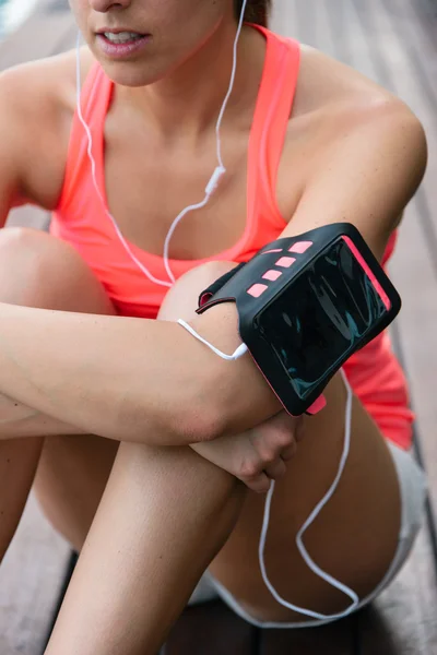 Sportiga kvinnan med hörlurar och mobiltelefon armband — Stockfoto