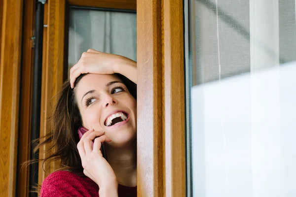 Ευτυχισμένη γυναίκα στο κινητό τηλέφωνο στο παράθυρο του σπιτιού — Φωτογραφία Αρχείου