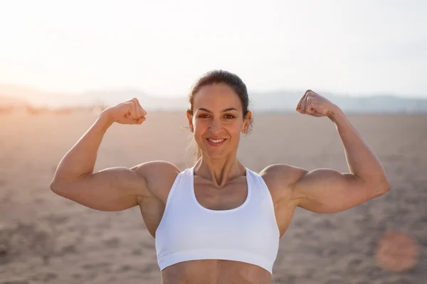 Strong fitness woman flexing biceps on sunset