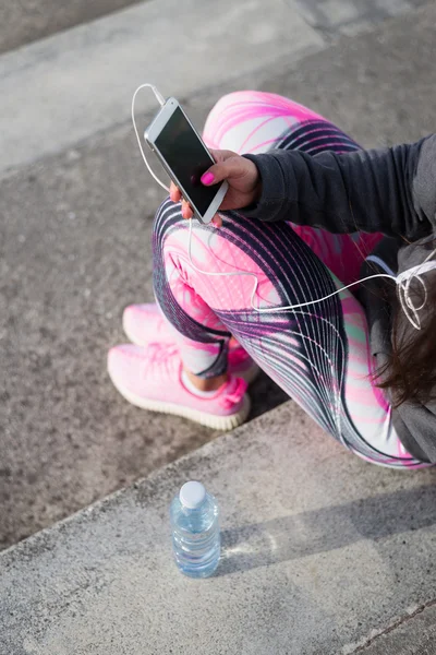 Sportiga kvinnan ta ett träningspass vila för textning på smartphone — Stockfoto