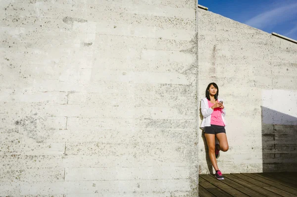 Asian athlete leaning against wall with smartphone — Stock Photo, Image