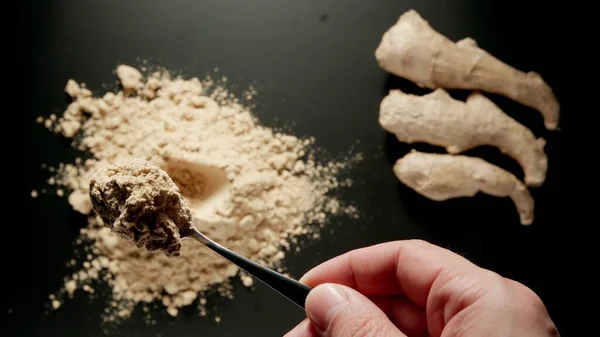 Male hand taking a teaspoon of ginger powder from a pile, top view