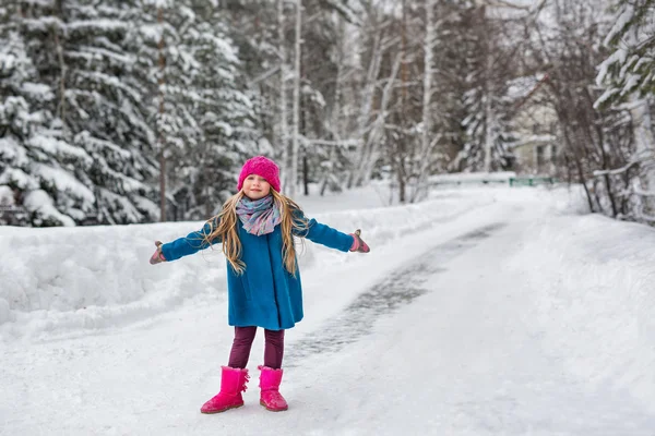 Little girl dressed in a blue coat and a pink hat and boots, hamming and playing in the winter forest