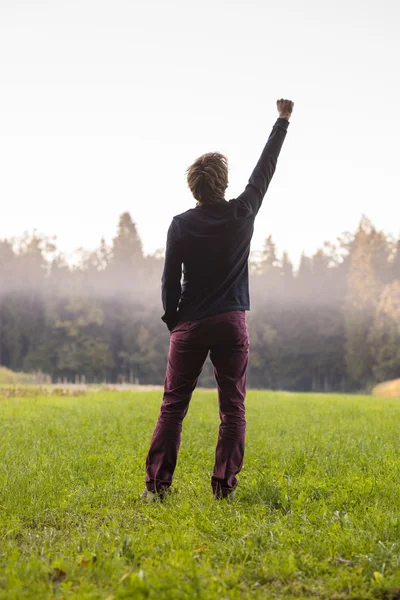 Rear view of a man standing in green meadow with one arm lifted — Stock Photo, Image