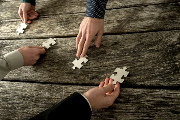 Hands of four businessman placing each a piece of puzzle in a ro — Stock Photo, Image