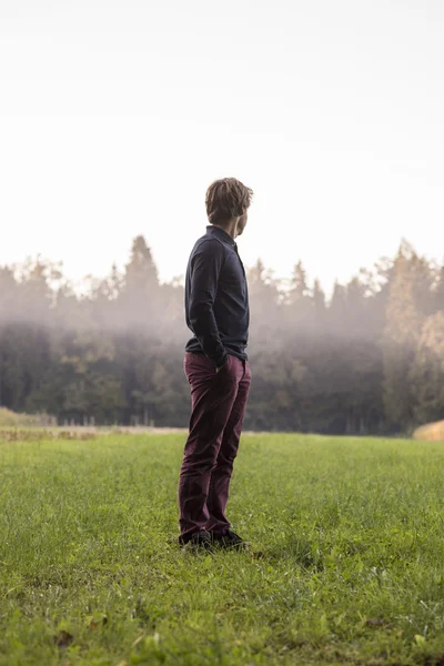 Joven de pie en el prado verde mirando a la distancia — Foto de Stock