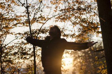 Young man in winter jacket standing with his arms spread widely 