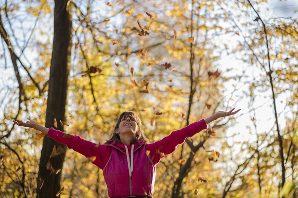 Gelukkige jonge vrouw gooien bladeren in de lucht — Stockfoto