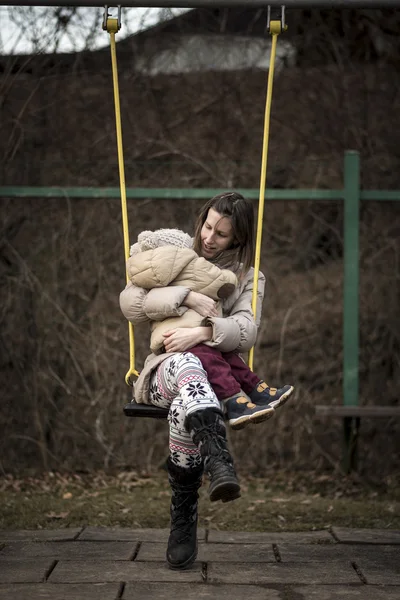 Madre disfrutando en un columpio en un parque con su niño pequeño en su regazo — Foto de Stock