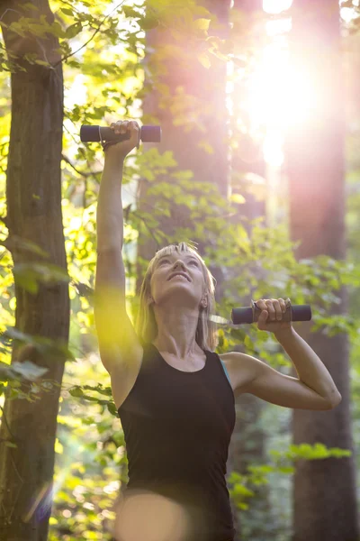 Tineri blonda femeie working afară cu gantere afară în foreste — Fotografie, imagine de stoc