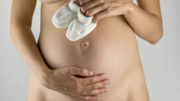 Zwangere vrouw bedrijf witte laarsjes — Stockfoto