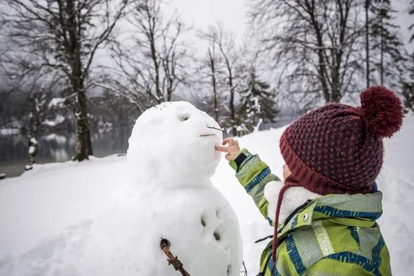 Criança fazendo um boneco de neve de inverno — Fotografia de Stock