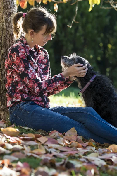 Mulher sentada debaixo de uma árvore acariciando seu cão — Fotografia de Stock