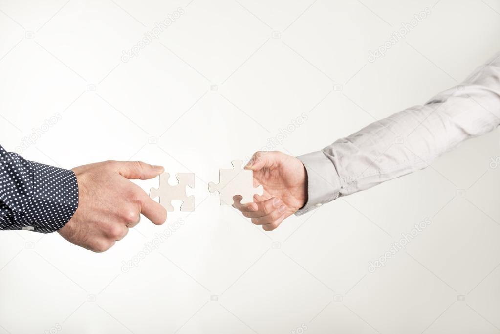 Two businessmen holding out puzzle pieces