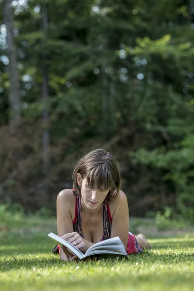 Erwachsene Frau liegt auf Gras und liest — Stockfoto