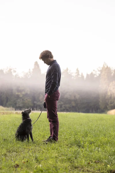 Homem na frente de bosques nebulosos com cão — Fotografia de Stock