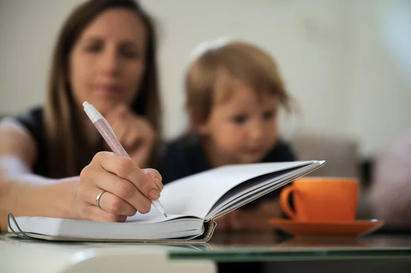 Νεαρή Μητέρα Γράφει Στο Σημειωματάριο Παιδί Της Δίπλα Της — Φωτογραφία Αρχείου